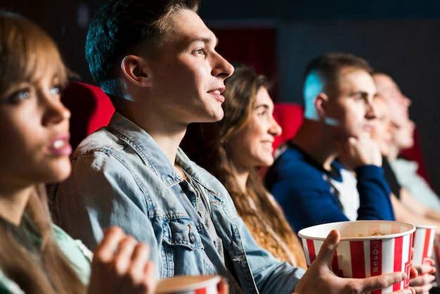Pessoas sentadas em poltronas, segurando pipocas, com expressões de expectativa, como se estivessem aguardando o início de um filme, simbolizando o evento do Cinedebate. A imagem faz alusão a um dos serviços prestados na Clínica de Psicologia Elísios.